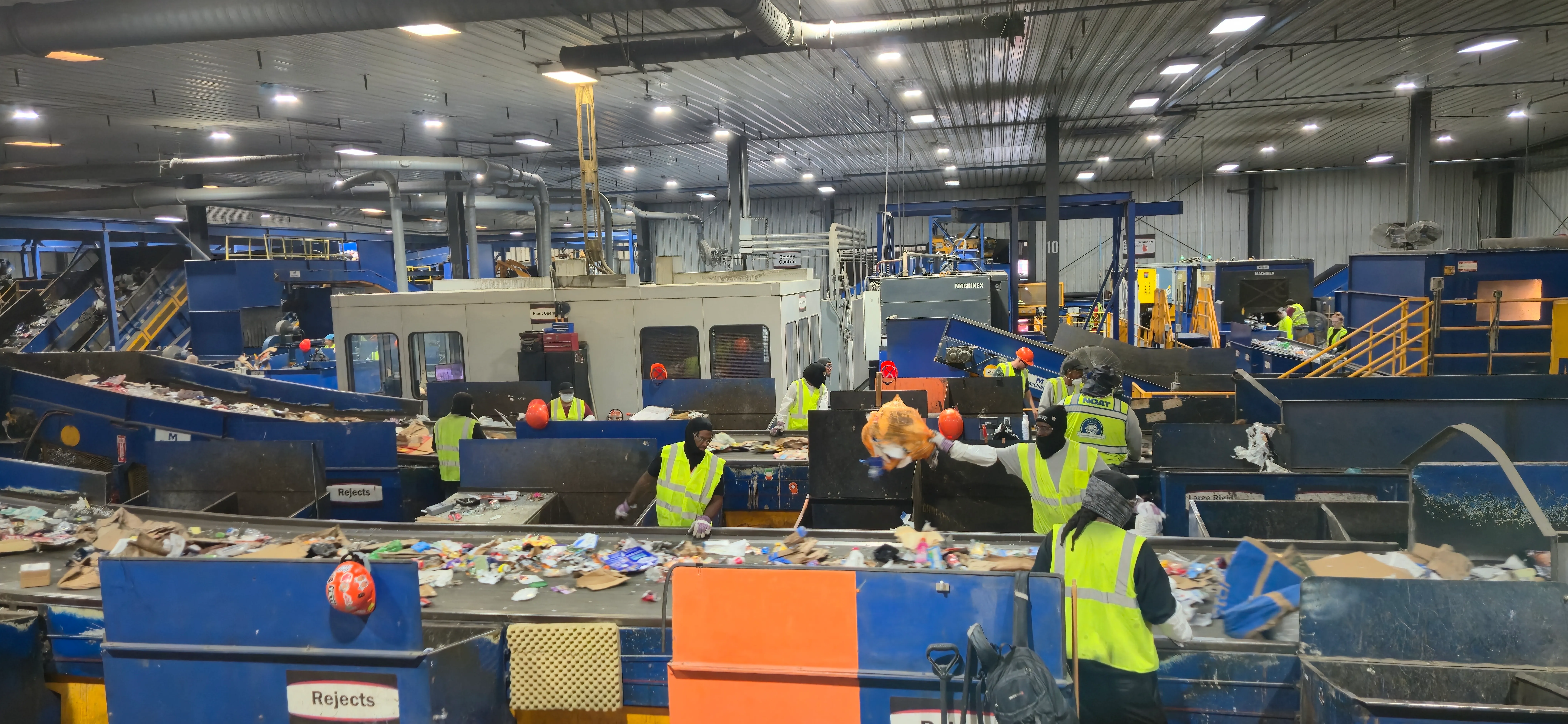 A high-angle view of Rumpke's sorting floor: conveyor belts crowded with mixed recyclables and workers in neon safety vests